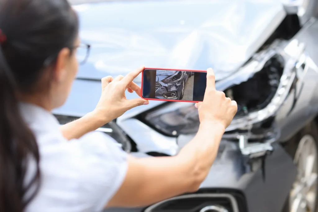 Woman taking a photo of her damaged car after a crash, demonstrating how to document evidence for a car accident injury claim.
