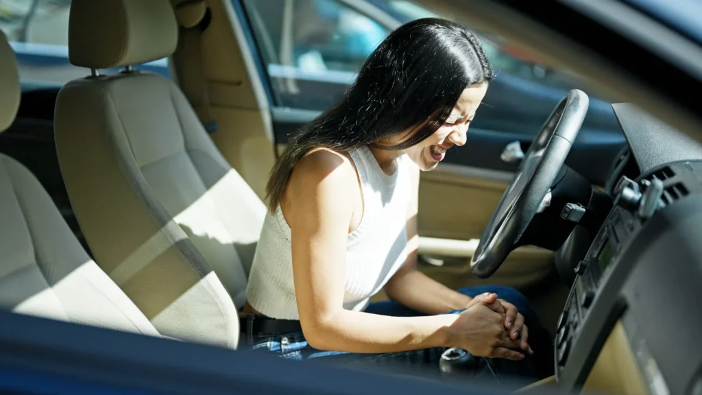 Young woman holding her knee in pain while sitting in a car, emphasizing the importance of seeing a doctor promptly after an auto accident.