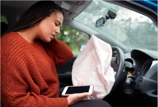 Woman in visible pain after airbag deployment, holding her phone in the driver’s seat—depicting soft tissue injuries treated by Oklahoma accident clinics.