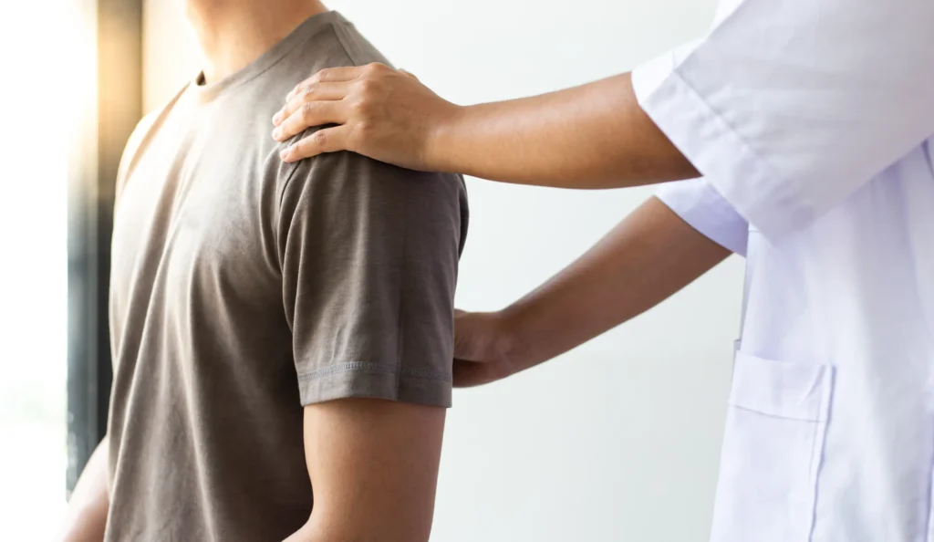 Chiropractor adjusting a male patient’s shoulder during a therapy session, focusing on upper body care and alignment.