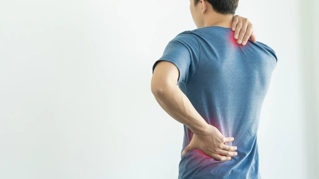 Man holding his lower back and neck in discomfort, highlighting areas of pain, commonly treated through chiropractic care.