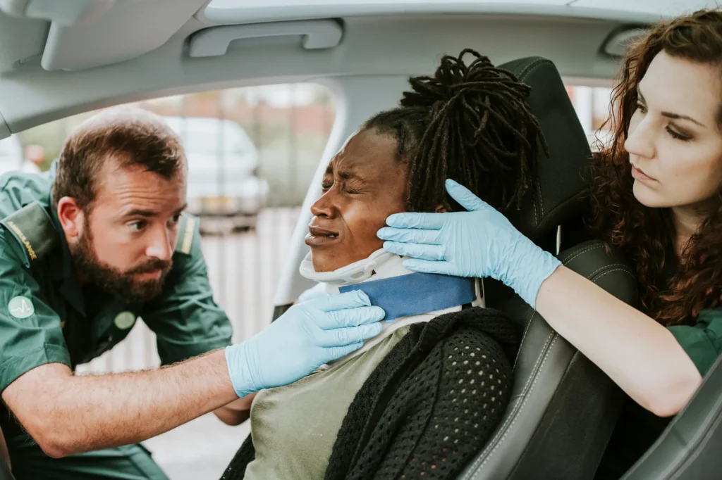 Injured woman wearing a neck brace while being assisted by paramedics in a car, highlighting emergency care often required before chiropractic treatment.